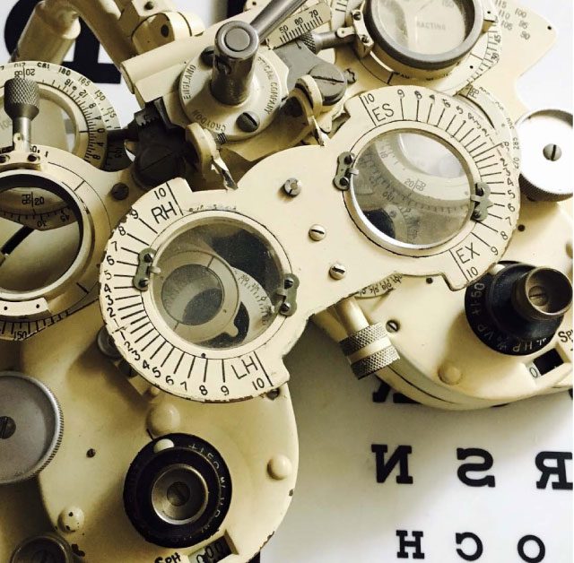 A phoropter over a test chart. The graded lens, the human eye behind it.